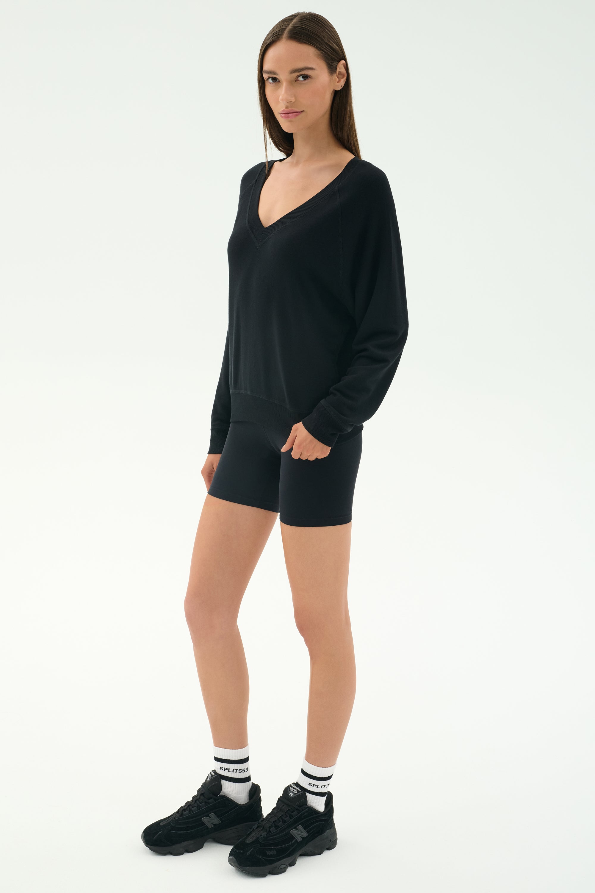 A woman wears the SPLITS59 Bennie Fleece V Neck Sweatshirt in black and shorts, made in Los Angeles.