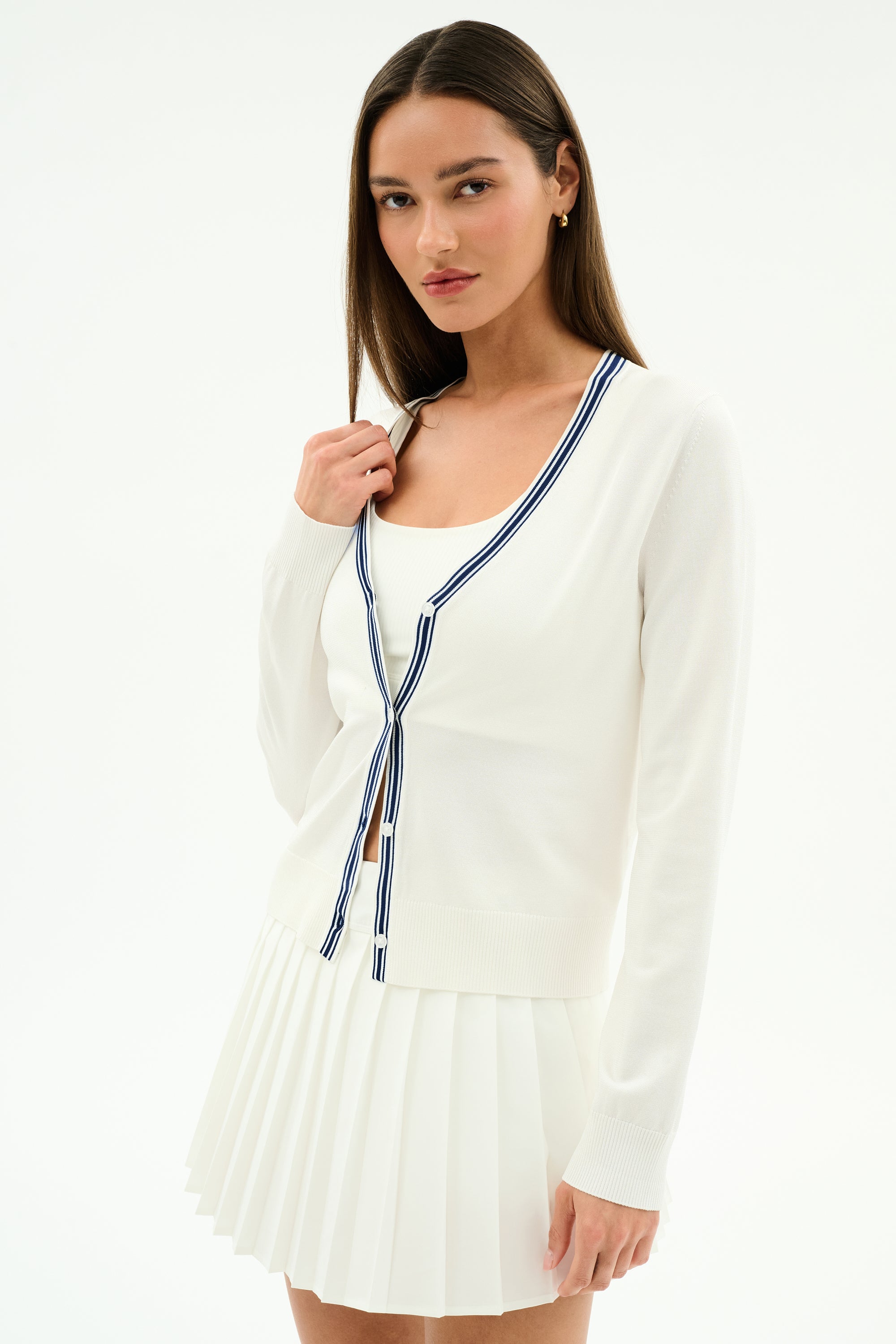 A woman faces forward against a plain background, wearing the SPLITS59 Bekah Knit Cardigan in White/Indigo over a white top and pleated skirt.
