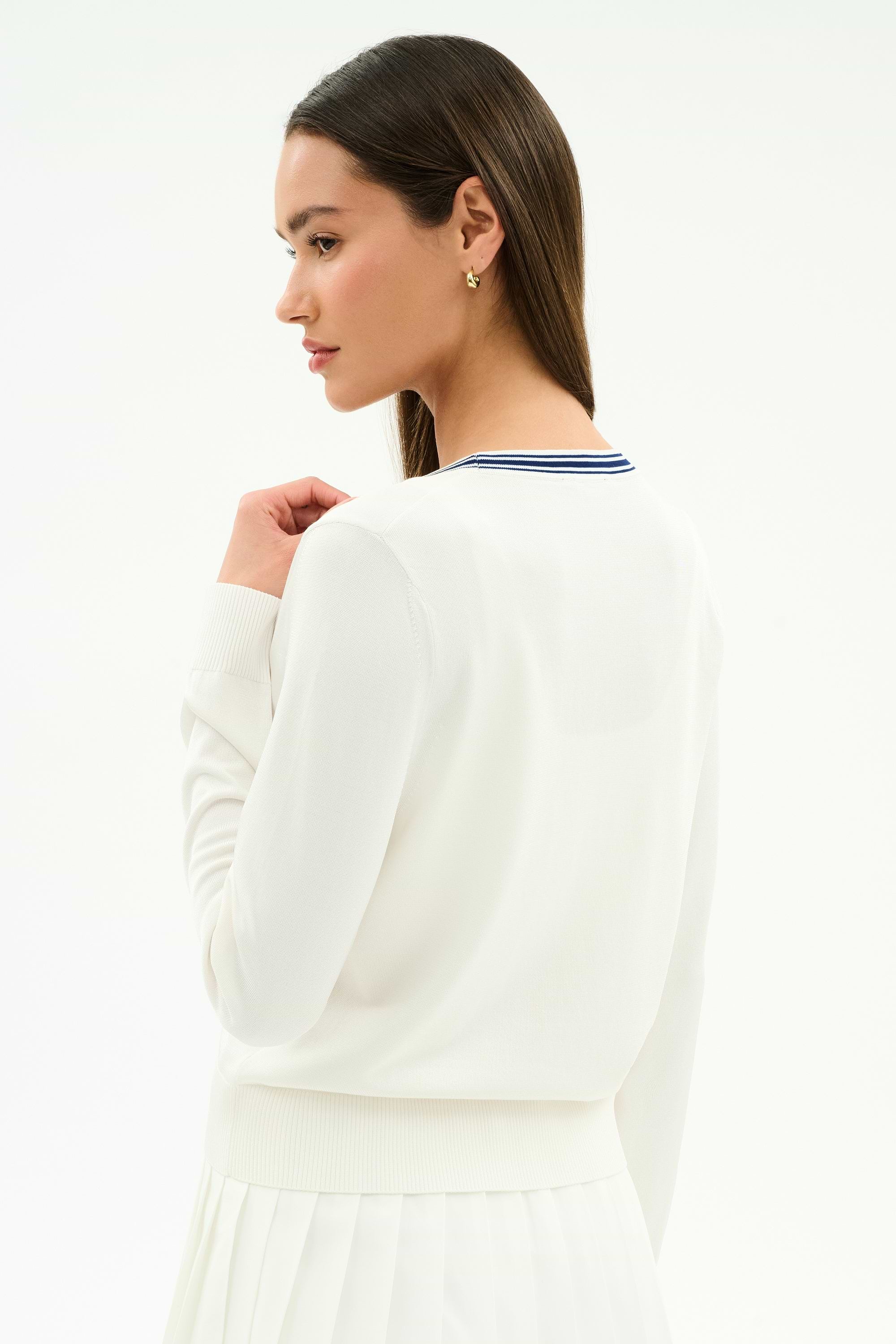 A woman with long brown hair wears the SPLITS59 Bekah Knit Cardigan in White/Indigo, featuring a blue-striped collar, and a white skirt, standing against a plain background shown from the back and in profile.