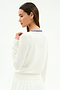 A woman with long brown hair wears the SPLITS59 Bekah Knit Cardigan in White/Indigo, featuring a blue-striped collar, and a white skirt, standing against a plain background shown from the back and in profile.