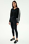 A woman stands in a studio wearing the SPLITS59 Ellie Fleece V Neck Sweatshirt in black/white, paired with black leggings and sneakers.