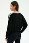 A woman stands with one hand on her hip, modeling the SPLITS59 Ellie Fleece V Neck Sweatshirt in Black/White and black spandex blend leggings, facing away from the camera against a plain background.
