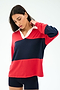 A person wears the SPLITS59 Katie Fleece Rugby in Pirate Red/Indigo with navy shorts, standing against a white background and looking down while touching their neck.
