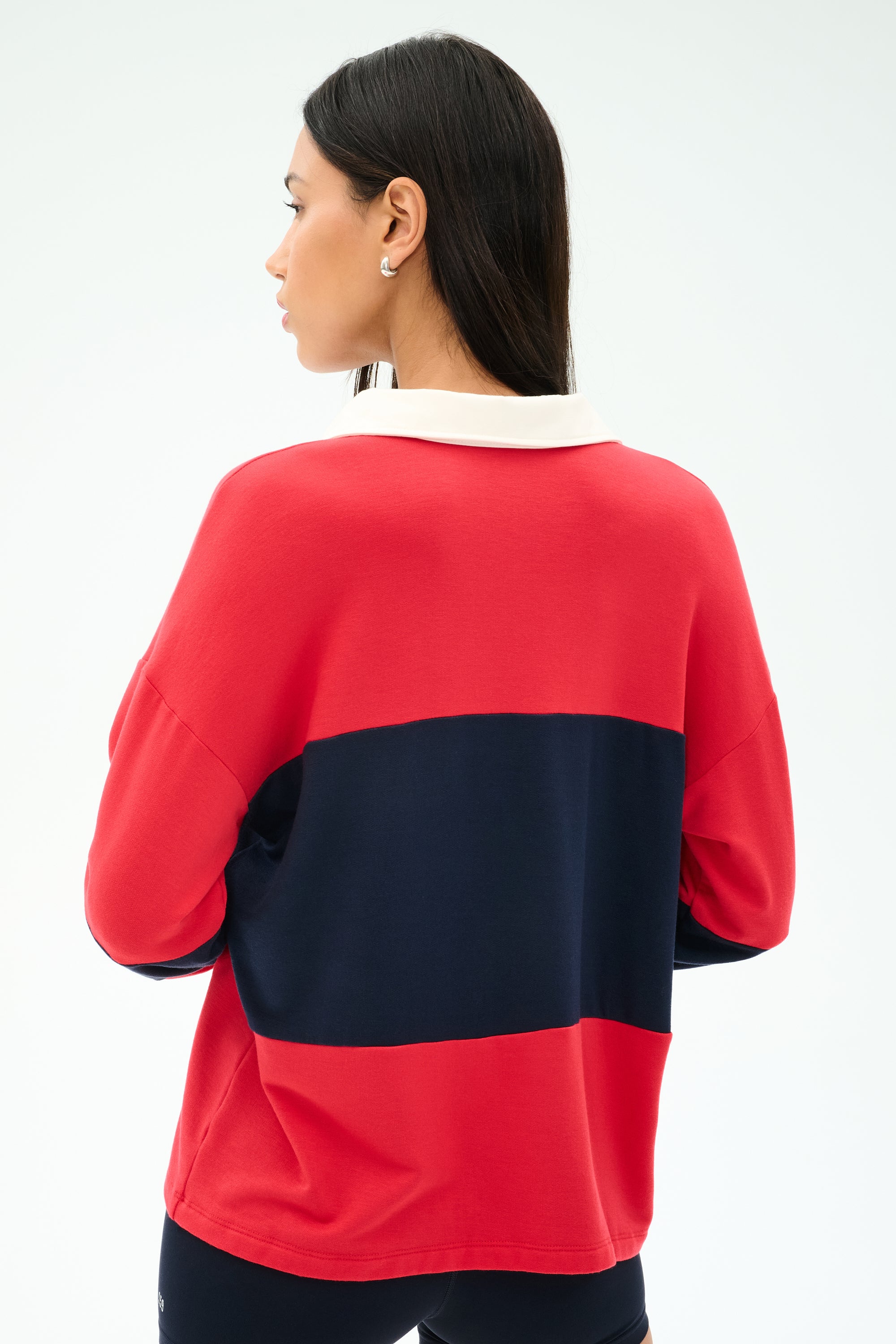 A woman with long dark hair, seen from the back, wears the SPLITS59 Katie Fleece Rugby in Pirate Red/Indigo with a white collar.