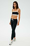 Dressed in a black and white sports bra, SPLITS59 Sonja Fleece Sweatpant - Black, and silver sneakers, this person stands against a plain background—ideal for cool weather workouts.