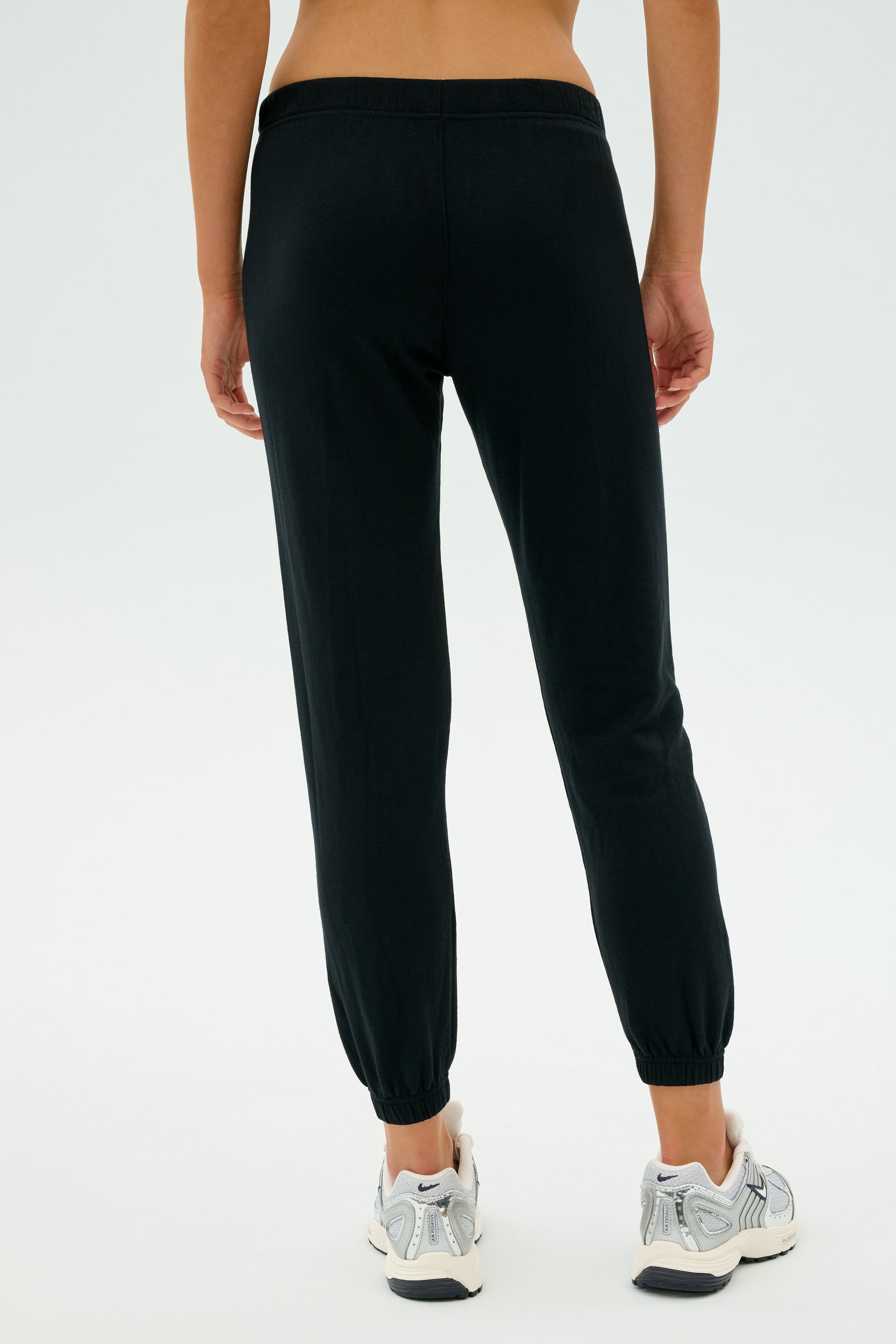 A person is shown from the back, standing against a light background in SPLITS59's Sonja Fleece Sweatpant - Black and white sneakers, ideal for cool weather workouts.