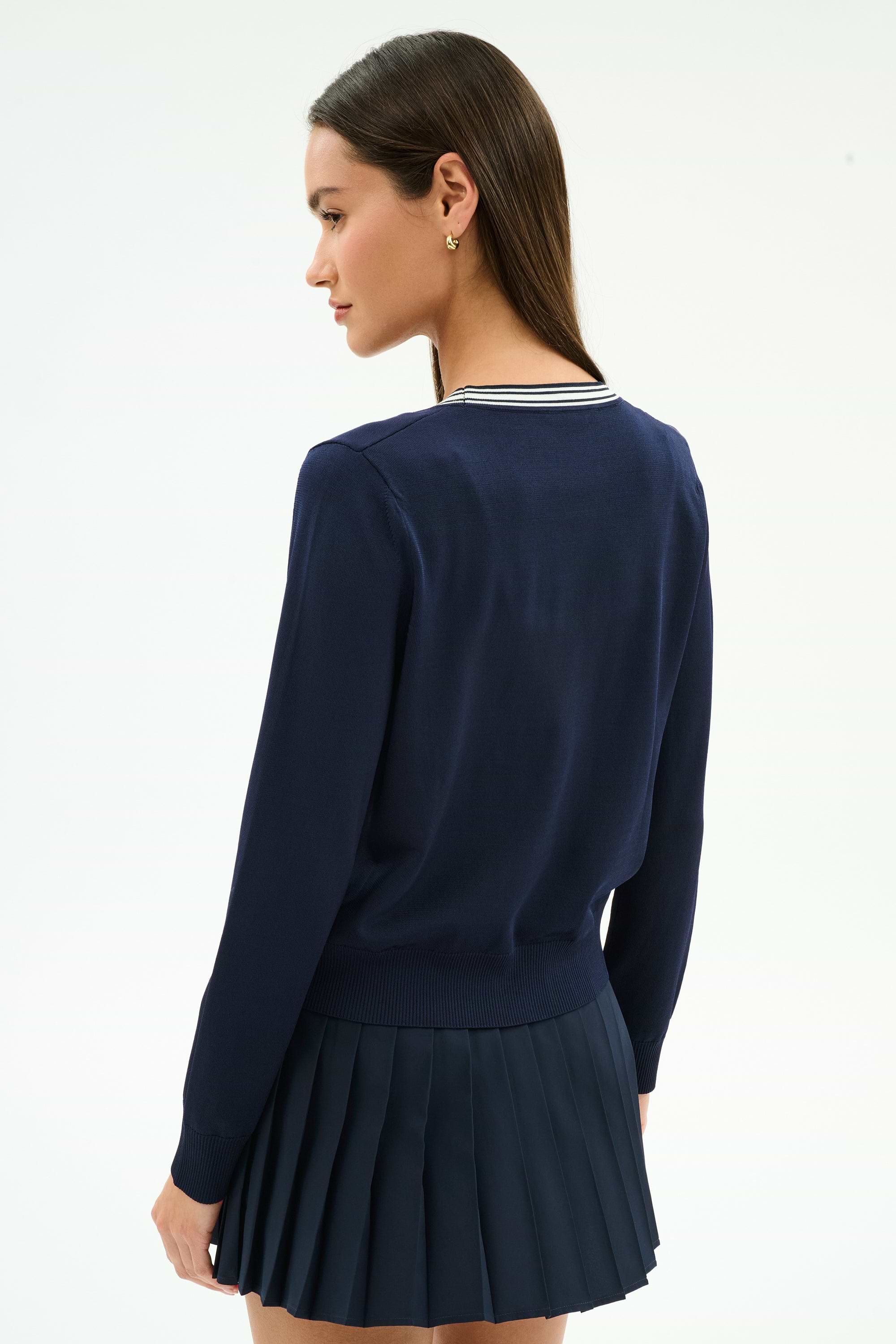 A woman with long brown hair, wearing the SPLITS59 Bekah Knit Cardigan in Indigo/White, stands turned slightly to the side against a plain light background.