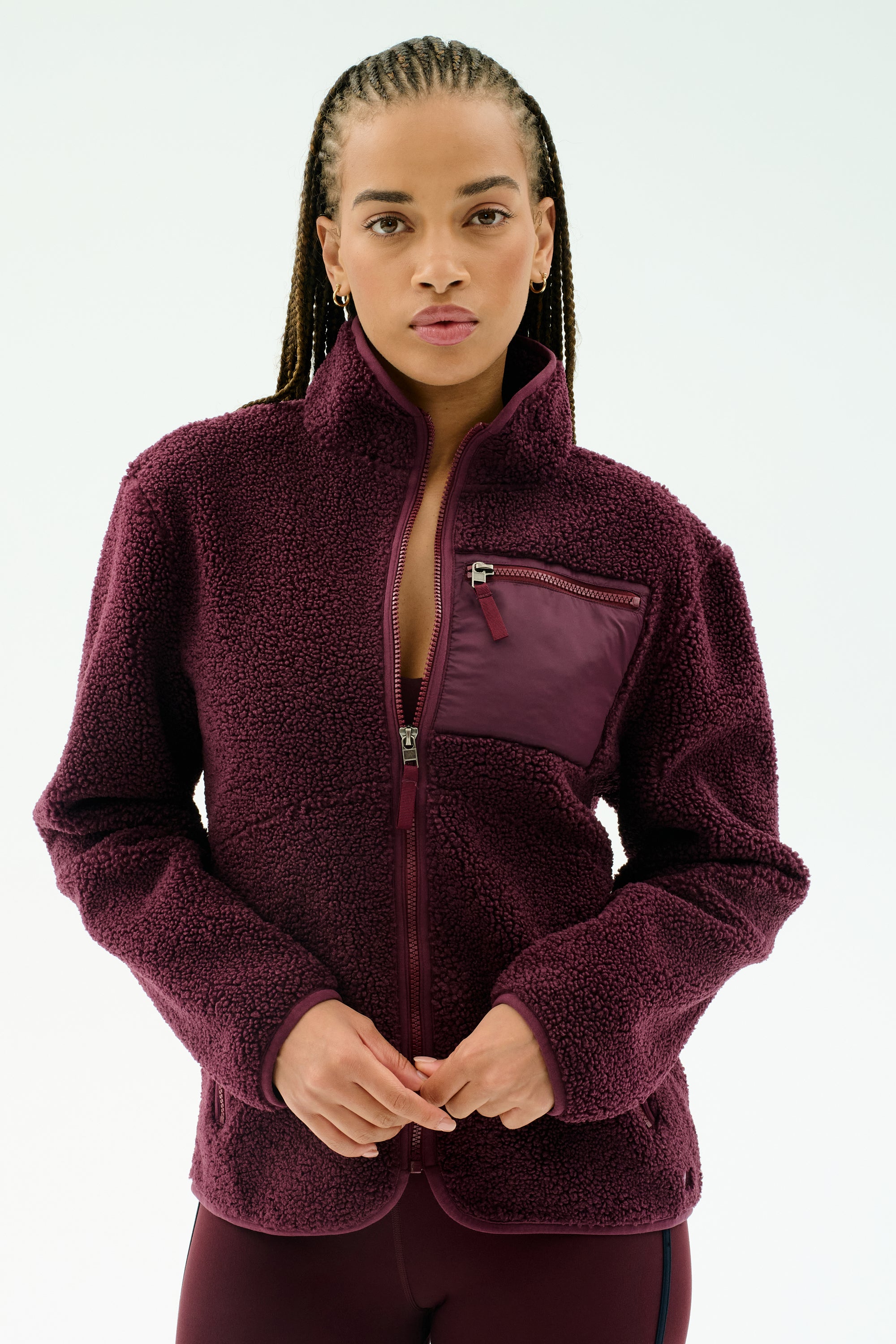 A person wearing the SPLITS59 Harris Sherpa Jacket in Dark Cherry, made from soft 100% polyester with a zippered chest pocket, stands against a plain light background.
