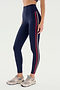 A person wears SPLITS59's Ella High Waist Airweight 7/8 leggings in Indigo/P Red with beige sneakers, standing against a white background, poised for hot yoga.