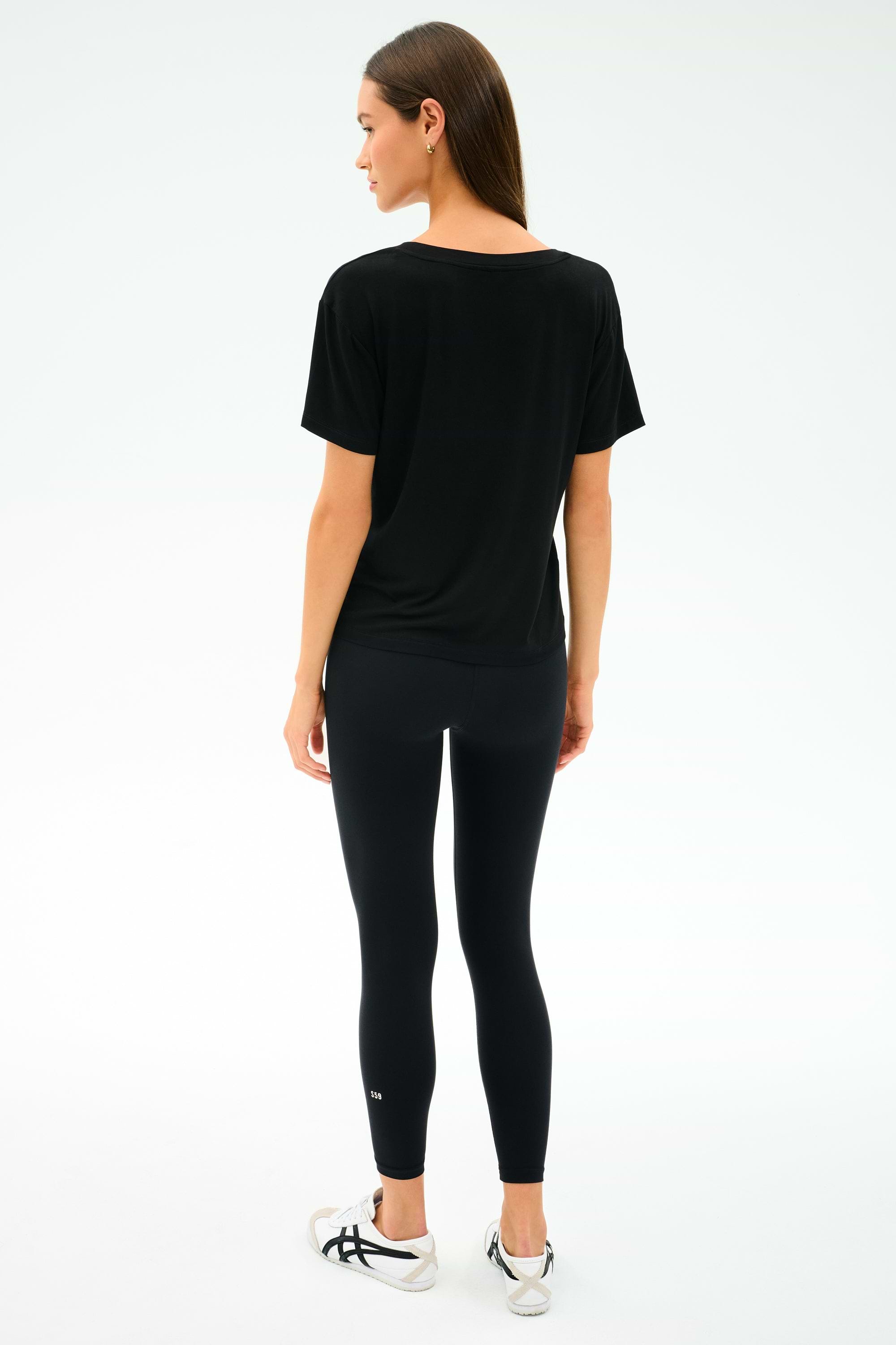 A woman faces away, wearing the SPLITS59 Georgia Jersey V-Neck in black, paired with black leggings and white sneakers against a light background.