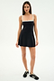 A woman faces forward in the SPLITS59 Monah Rigor Dress - Black/White, a sleeveless style with white trim, paired with black Adidas sneakers against a plain white background.