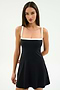 A woman models the SPLITS59 Monah Rigor Dress in Black/White, a chic sleeveless style with white straps and trim, set against a plain light background.