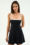 A woman models the SPLITS59 Monah Rigor Dress in Black/White, a chic sleeveless style with white straps and trim, set against a plain light background.