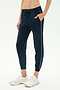 A person wears SPLITS59’s Airweight Jogger 7/8 with Piping in Indigo/White, featuring a relaxed fit, white trim, drawstring waist, and white sneakers. The cropped image shows hands in pockets—ideal for light workouts.