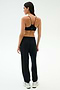 A woman stands with her back to the camera in SPLITS59’s Andie Oversized Fleece Varsity 59 Sweatpant - Black/59, paired with a black sports bra and white sneakers, ideal for cool weather workouts against a plain light background.