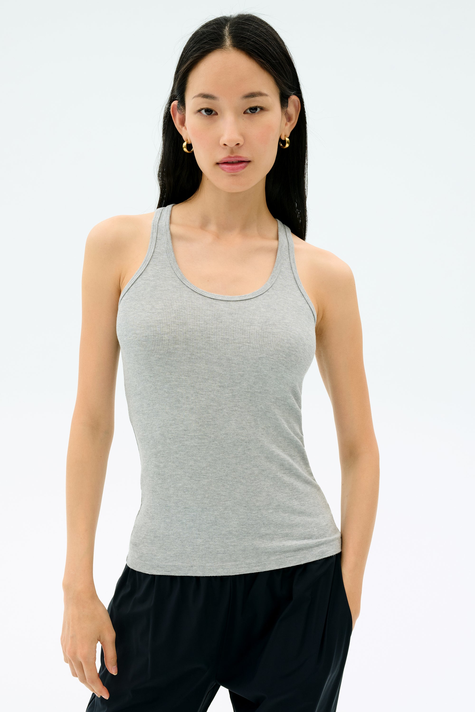A woman wearing the Splits59 Ashby Rib Tank in Lt. Heather Grey and black pants stands against a plain light background, facing forward with a neutral expression.