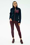A person stands facing forward wearing the SPLITS59 Harris Sherpa Jacket in Indigo/Dark Cherry, featuring 100% polyester and a maroon chest pocket, along with maroon leggings and sneakers against a plain white background.