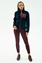 A person stands facing forward wearing the SPLITS59 Harris Sherpa Jacket in Indigo/Dark Cherry, featuring 100% polyester and a maroon chest pocket, along with maroon leggings and sneakers against a plain white background.