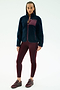 A person stands facing forward wearing the SPLITS59 Harris Sherpa Jacket in Indigo/Dark Cherry, paired with burgundy leggings and sneakers, against a plain white background.