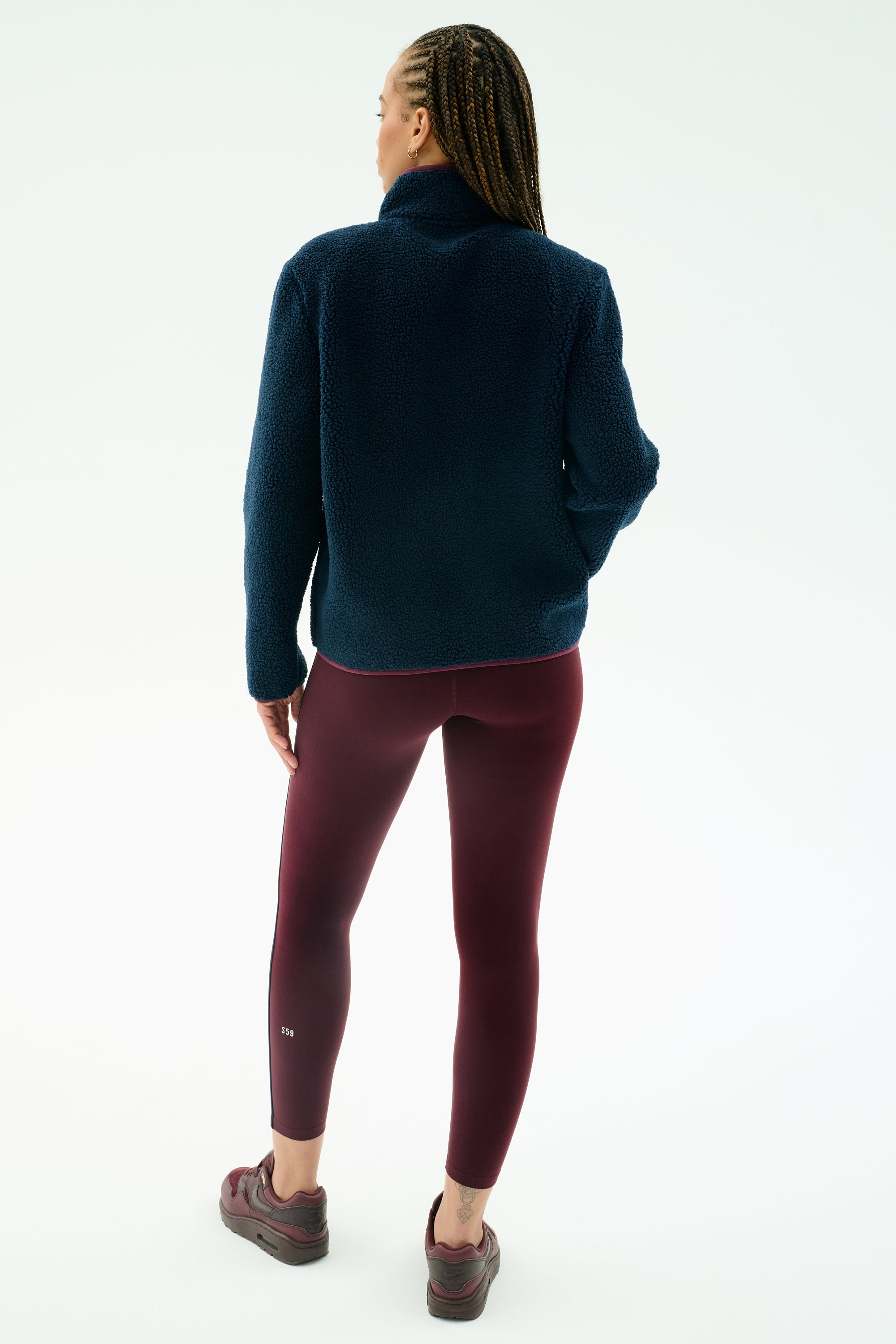 A person faces away, wearing the SPLITS59 Harris Sherpa Jacket in Indigo/Dark Cherry, paired with burgundy leggings and sneakers, set against a plain light background.