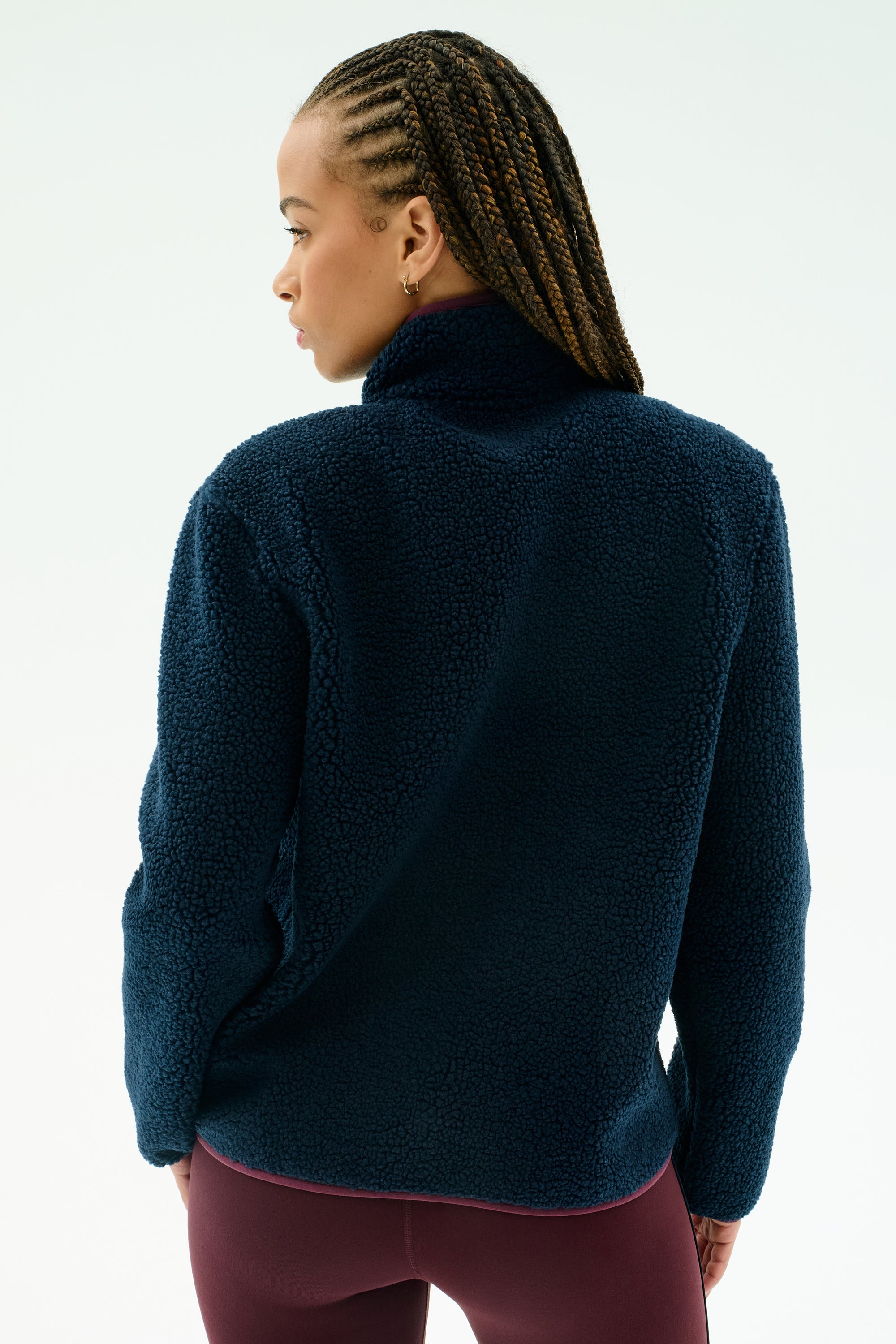 A person with braided hair is seen from the back wearing the SPLITS59 Harris Sherpa Jacket in Indigo/Dark Cherry, paired with burgundy pants, set against a plain light background.