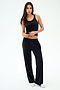 A woman stands against a plain background wearing the SPLITS59 Mel Airweight Lite Tank in black, paired with black wide-leg pants and white sneakers.