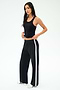 A woman stands against a plain background wearing the SPLITS59 Mel Airweight Lite Tank in black, paired with black wide-leg pants featuring a white side stripe, and white sneakers.