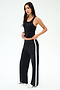 A woman stands against a plain background wearing the SPLITS59 Mel Airweight Lite Tank in black, paired with black wide-leg pants featuring a white side stripe, and white sneakers.