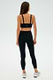 A woman models the SPLITS59 Monah Rigor Bra - Black, paired with black leggings and white sneakers, against a simple, light backdrop.
