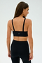 A woman in black athletic wear, wearing the SPLITS59 Monah Rigor Bra - Black, turns away, highlighting the sleek design of her sports bra and leggings against a plain backdrop—ideal for intense gym workouts.