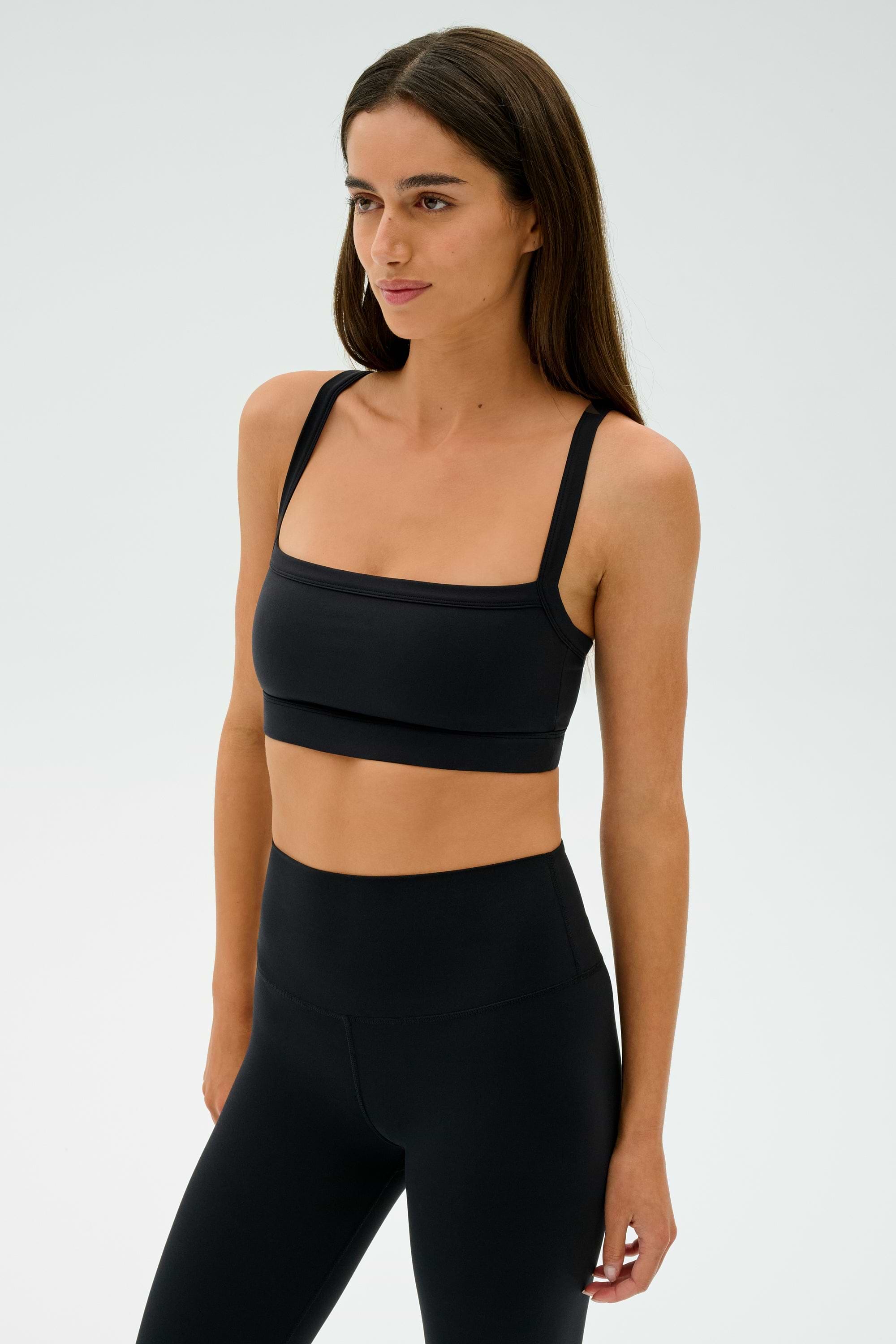 A person in black athletic wear, including SPLITS59's Monah Rigor Bra - Black, stands against a plain background embodying the spirit of intense gym workouts.