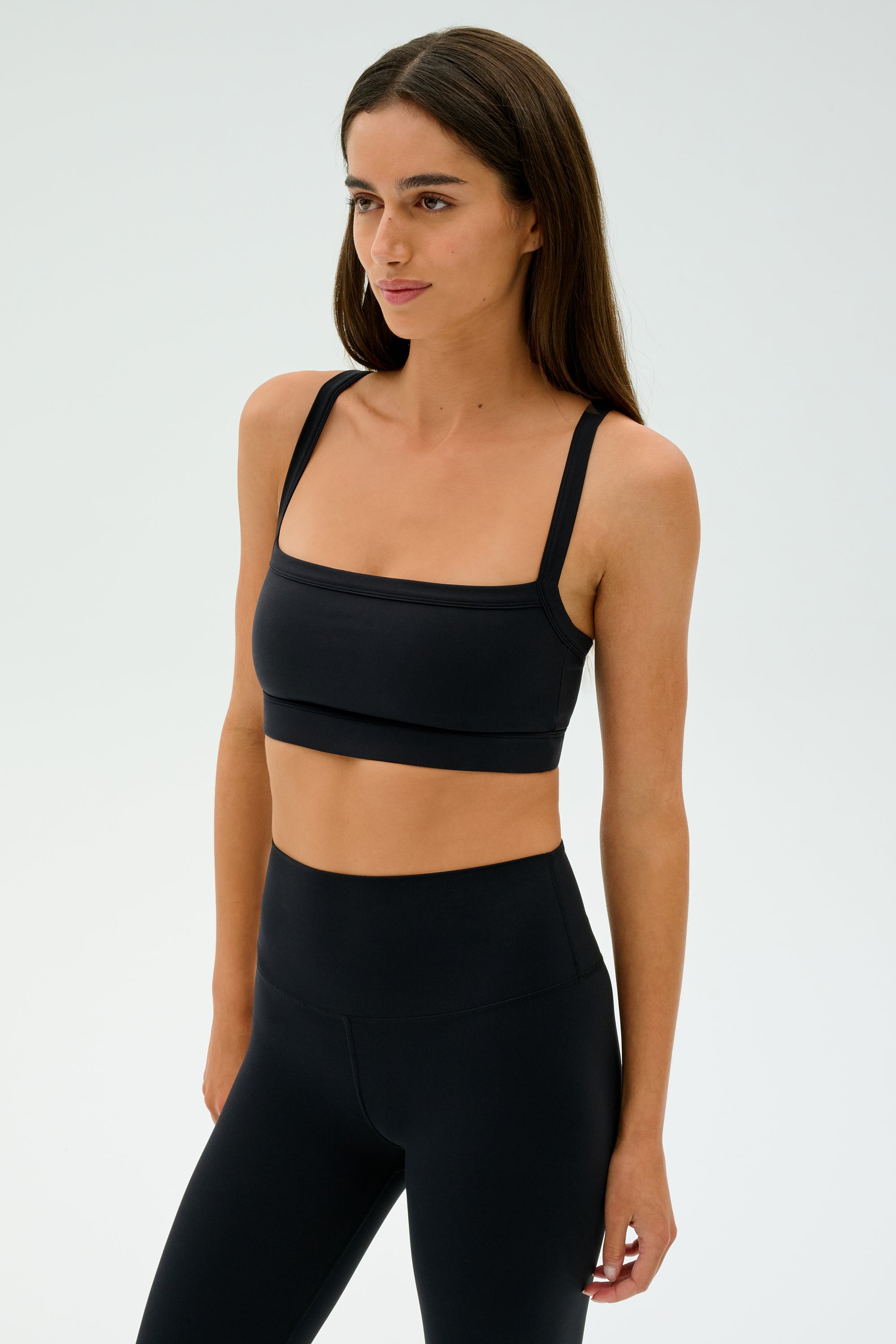 A person in black athletic wear, including SPLITS59's Monah Rigor Bra - Black, stands against a plain background embodying the spirit of intense gym workouts.