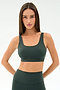 A woman with long brown hair wears the SPLITS59 Airweight Rib Bra in Military and matching high-waisted leggings, made from soft nylon spandex, standing with hands on hips against a plain white background.