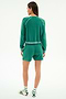 A person stands facing away on a plain light background, wearing the SPLITS59 Reena Fleece Sweatshort in Arugula with a matching green long-sleeve top, white socks featuring green stripes, and white sandals.