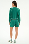 A person stands facing away on a plain light background, wearing the SPLITS59 Reena Fleece Sweatshort in Arugula with a matching green long-sleeve top, white socks featuring green stripes, and white sandals.
