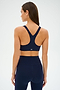 A person in SPLITS59's Ella Airweight Bra, Indigo/Black Currant, is set against a light background. Perfect for hot yoga sessions, this navy athletic outfit offers ultimate comfort and flexibility with its ultra-soft Airweight fabric and sleek racerback design.