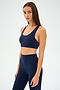A person in an Ella Airweight Bra by SPLITS59, in Indigo/Black Currant, stands against a plain background, exuding confidence and readiness for hot yoga.