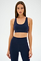 An individual in an Ella Airweight Bra by SPLITS59, in an Indigo/Black Currant color scheme, stands against a plain backdrop, highlighting its sleek racer back design.