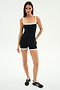 A woman stands against a plain background wearing the SPLITS59 Monah Rigor Jumpsuit in black/white—made from supportive Rigor fabric for high-impact workouts—and black sneakers with white stripes.