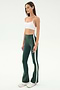 A woman wears the SPLITS59 Raquel High Waist Flared Legging in Military/White, paired with a white sports bra and white sneakers, standing against a plain background.