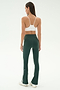 A woman faces away, wearing SPLITS59's Raquel High Waist Flared Legging in Military/White and a white sports bra, paired with white sneakers against a plain light background.