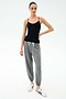 A woman stands against a white background wearing the SPLITS59 Loren Seamless Waist Length Tank in black, paired with gray drawstring jogger pants and white sneakers.