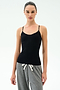 A person wears the SPLITS59 Loren Seamless Waist Length Tank in black, featuring a built-in shelf bra, paired with gray drawstring pants, standing against a plain white background.