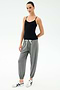 A person stands against a plain background wearing the SPLITS59 Loren Seamless Waist Length Tank in black, paired with gray drawstring sweatpants and white sneakers.
