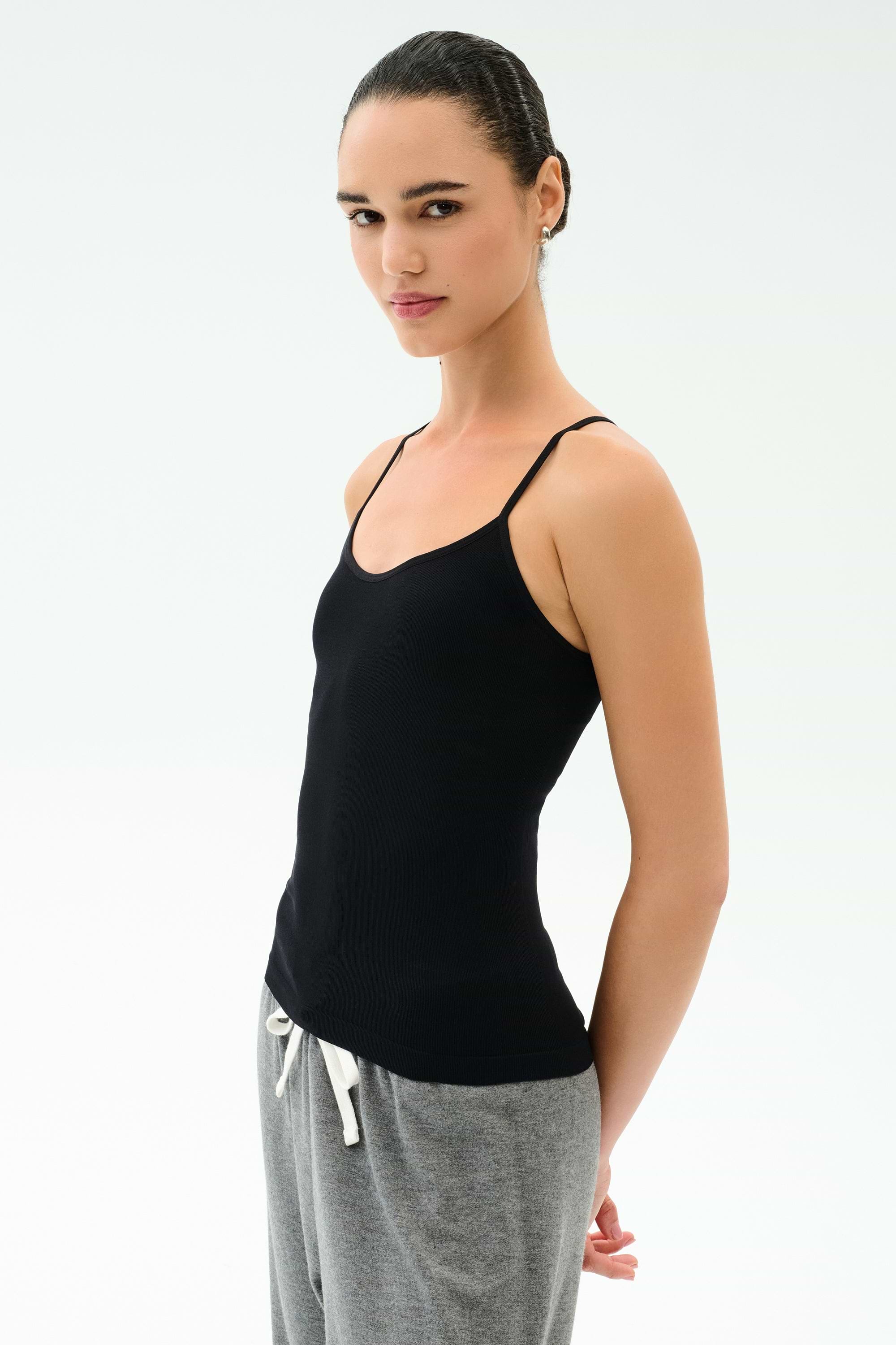 A person wears the SPLITS59 Loren Seamless Waist Length Tank in black and gray drawstring pants, standing slightly sideways against a white background.