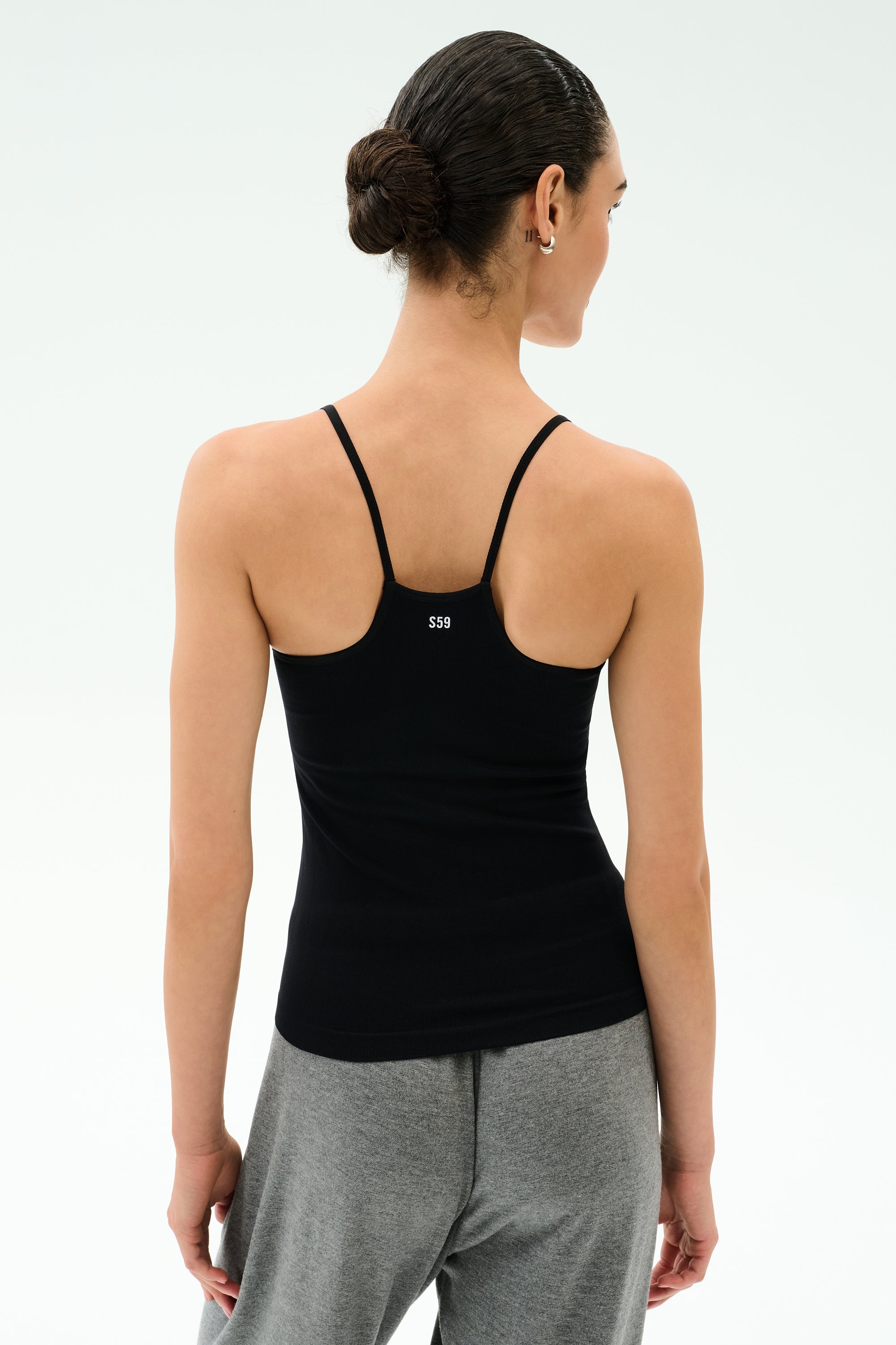 A person shown from the back wears the SPLITS59 Loren Seamless Waist Length Tank in black with gray pants, standing against a plain light background.