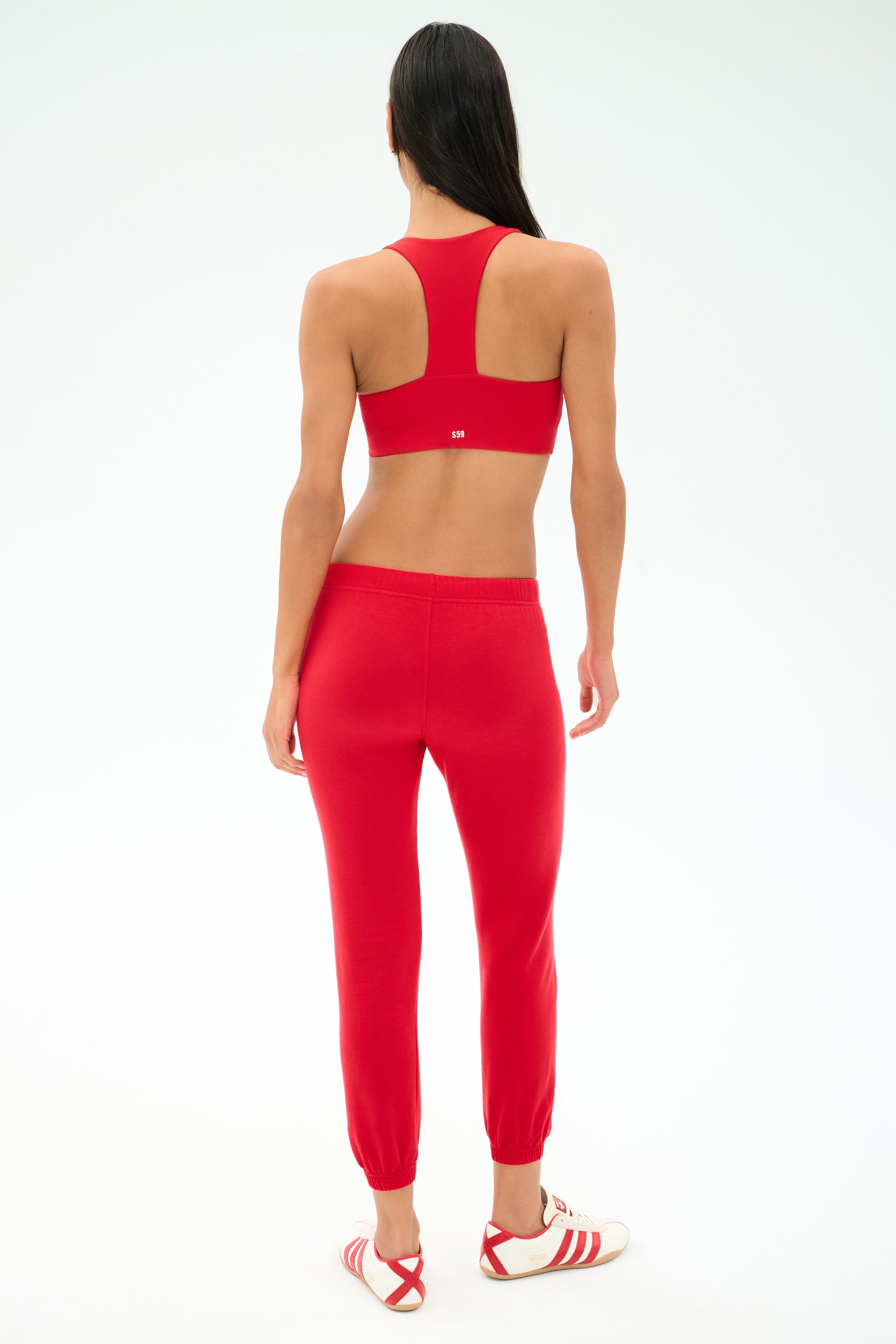 A person stands in Los Angeles facing away from the camera, wearing a red sports bra, SPLITS59 Sonja Fleece Sweatpant in Pirate Red, and white sneakers with red stripes.