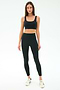 A woman stands facing forward, wearing the SPLITS59 Airweight Rib High Waist 7/8 leggings in black with a matching sports bra and white sneakers against a plain white background—ideal for Pilates or hot yoga.