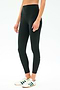 A person wears SPLITS59's Airweight Rib High Waist 7/8 leggings in black, ideal for Pilates or hot yoga, paired with white sneakers featuring green stripes, standing against a plain light background.