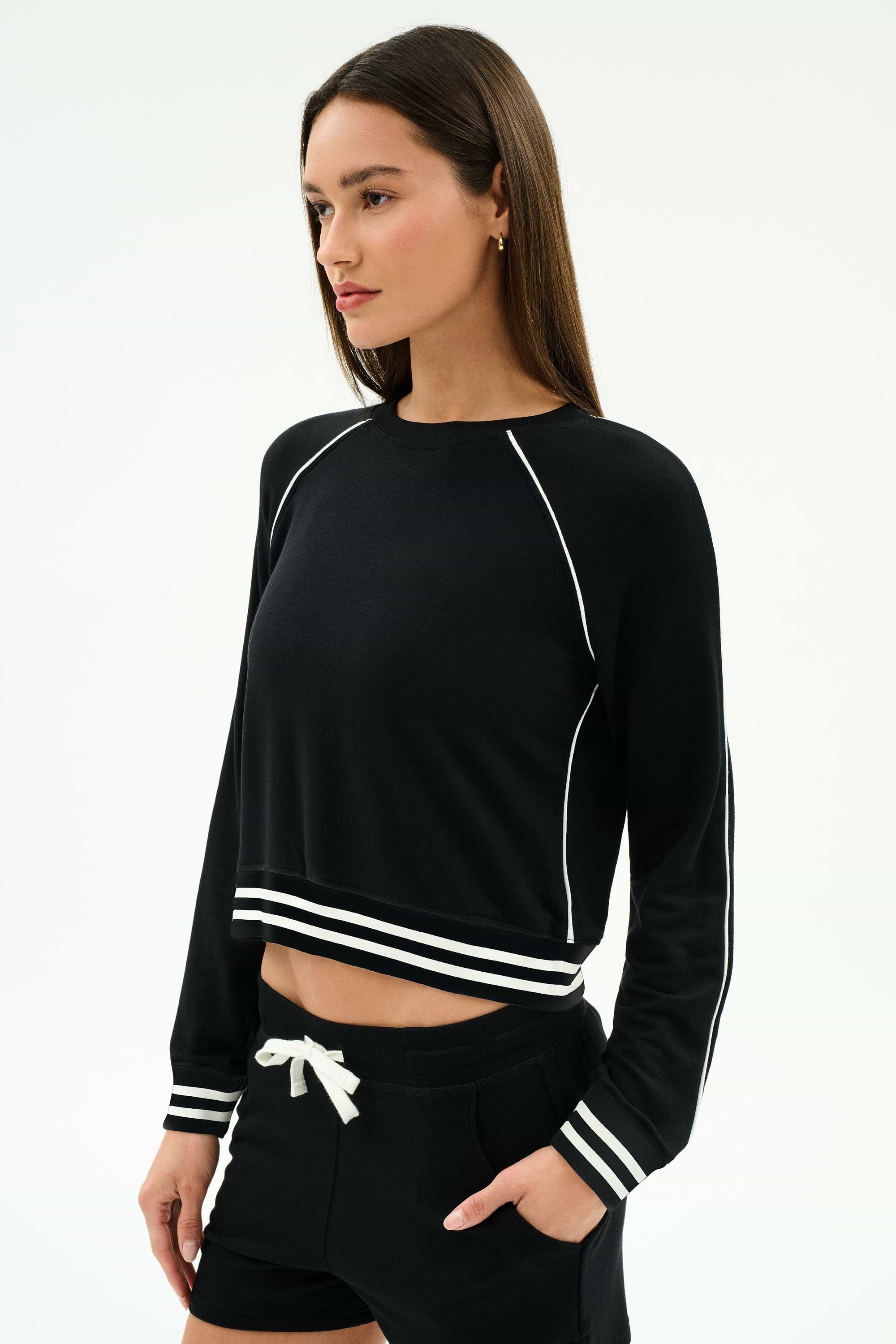 A woman wears the SPLITS59 Brooks Fleece Sweatshirt With Stripe in black/white, paired with matching black shorts, both crafted from soft modal fabric, as she stands against a plain white background.